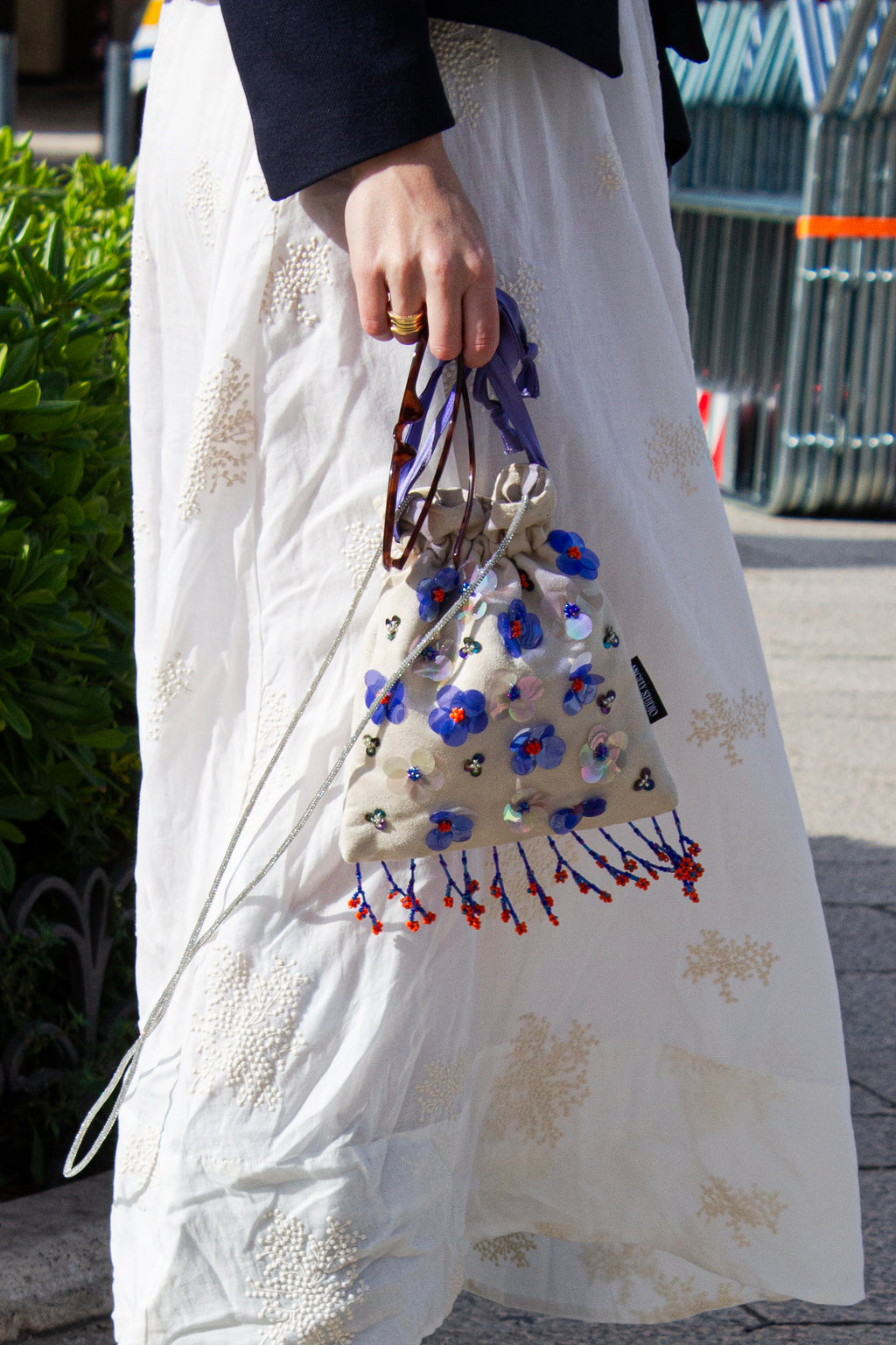 Handcrafted off-white suede drawstring bag with blue sequin flowers & beaded fringe. Internal pocket, 120cm strap, 24×22cm. Perfect for events & everyday glam.