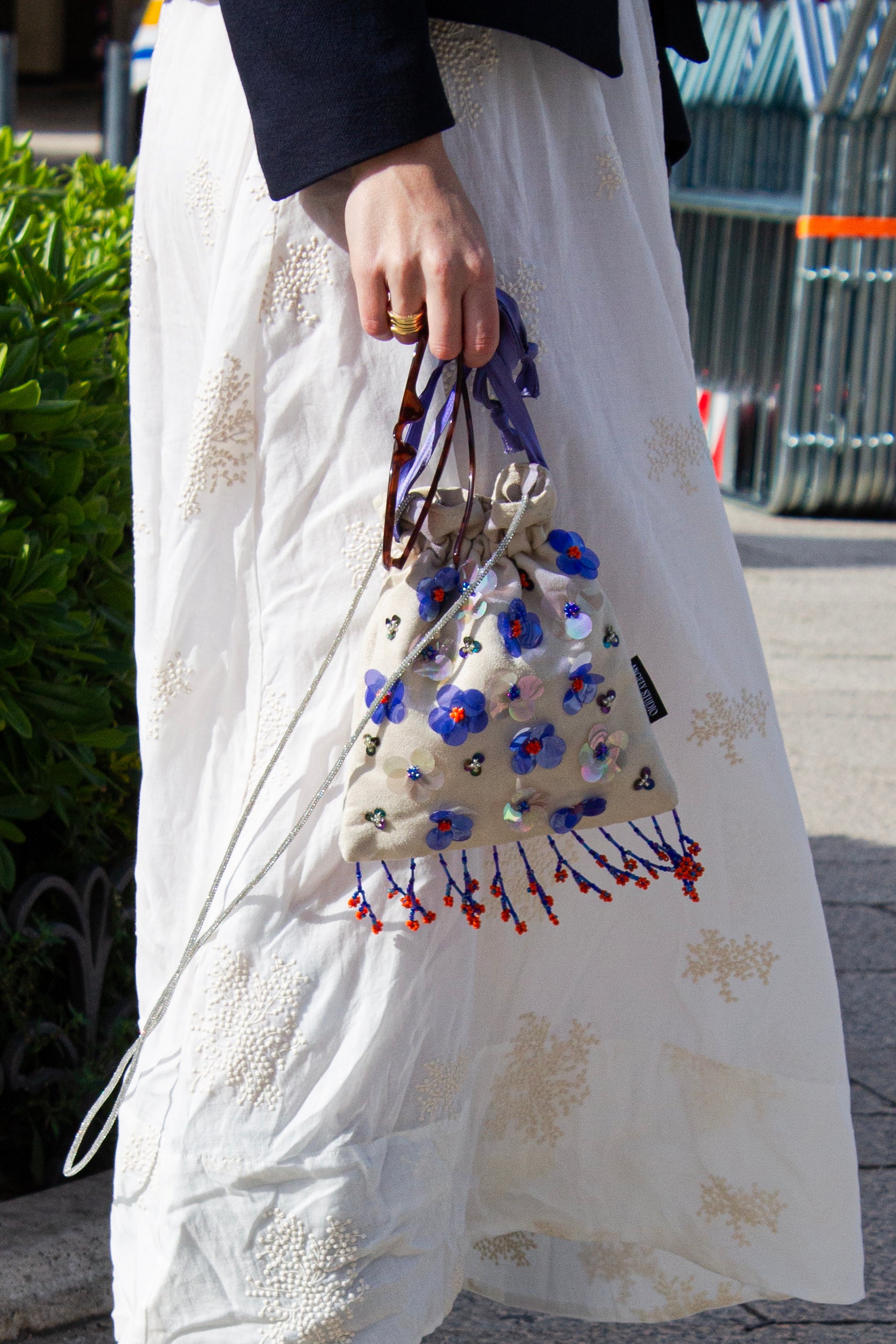 Handcrafted off-white suede drawstring bag with blue sequin flowers & beaded fringe. Internal pocket, 120cm strap, 24×22cm. Perfect for events & everyday glam.