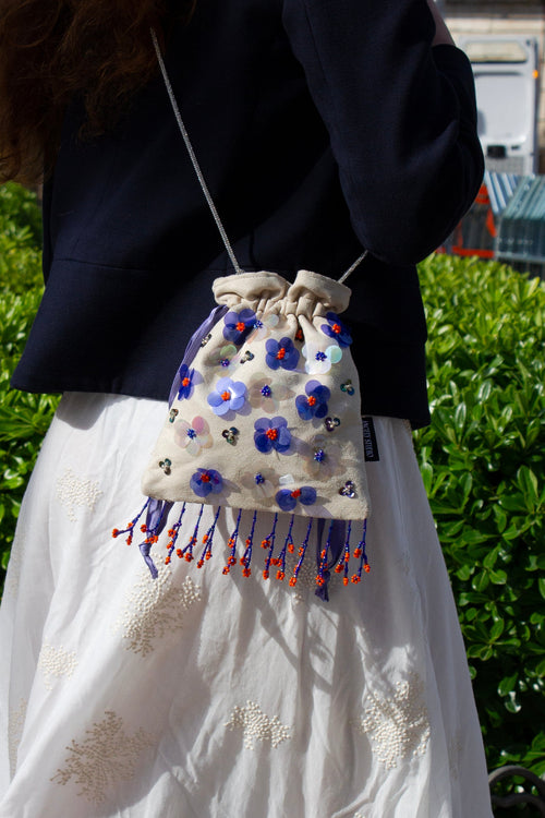 Handcrafted off-white suede drawstring bag with blue sequin flowers & beaded fringe. Internal pocket, 120cm strap, 24×22cm. Perfect for events & everyday glam.