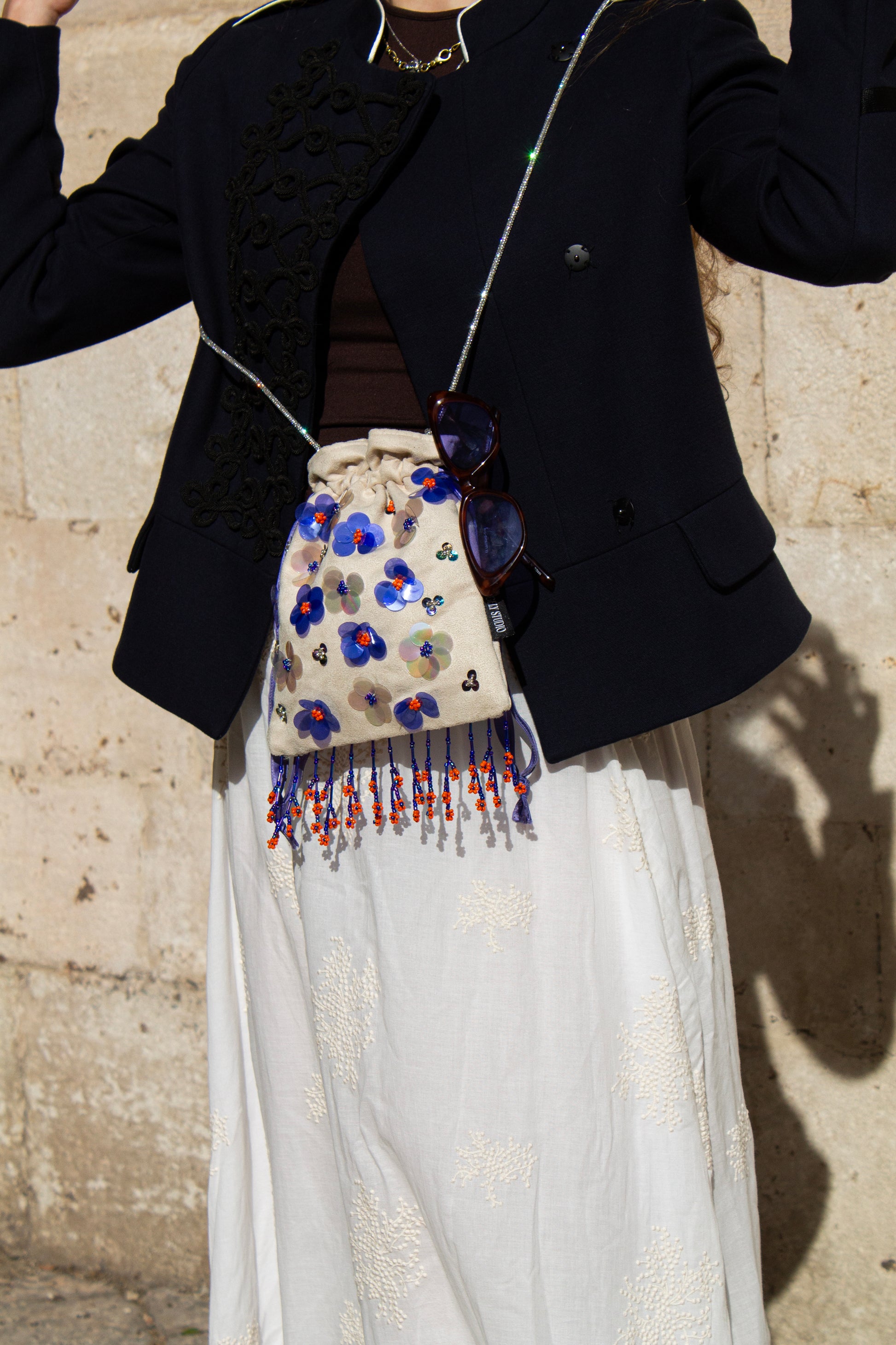 Handcrafted off-white suede drawstring bag with blue sequin flowers & beaded fringe. Internal pocket, 120cm strap, 24×22cm. Perfect for events & everyday glam