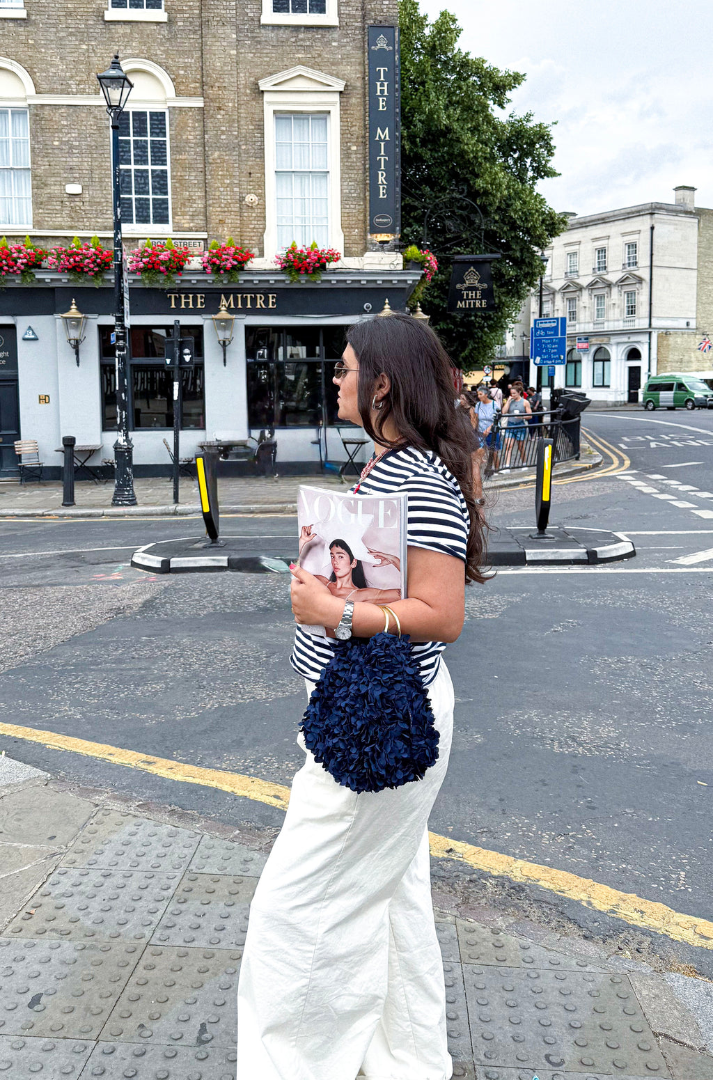 Woman holding a Vogue Magazine on a city street with buildings 