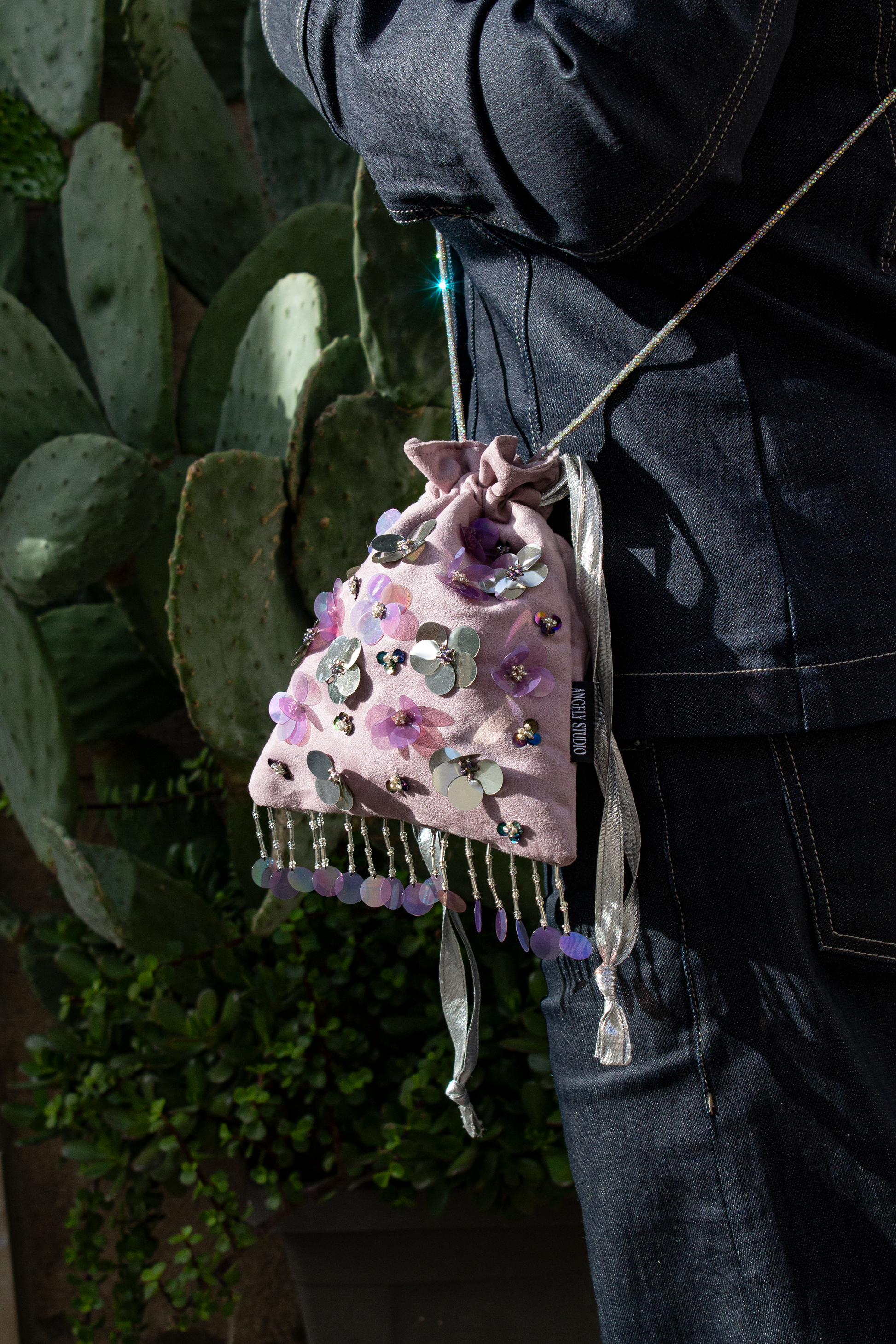 Handcrafted mauve suede drawstring bag with violet and silver sequin flowers & beaded fringe. Internal pocket, 120cm strap, 24×22cm. Perfect for events & everyday glam.